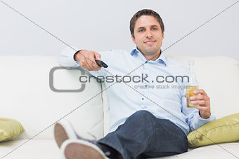 Man with a drink and remote control sitting on sofa at home