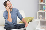 Cheerful man using cellphone and laptop in living room