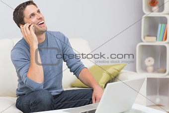 Cheerful man using cellphone and laptop in living room
