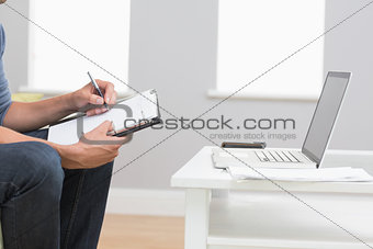 Mid section of a man with laptop writing in diary at home