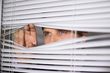Businessman peeking through blinds in office