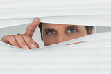 Close-up of green eyed businessman peeking through blinds