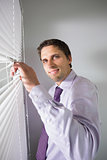 Portrait of businessman peeking through blinds in office