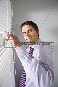 Portrait of businessman peeking through blinds in office
