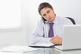 Businessman on call while writing in diary at office