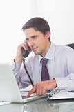 Businessman using telephone and laptop at desk