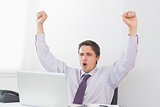 Businessman cheering in front of laptop in office