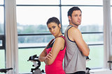 Serious young woman and man standing back to back in gym