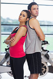 Serious woman and man standing back to back in gym