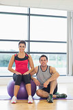 Young woman and man with fitness ball sitting at gym