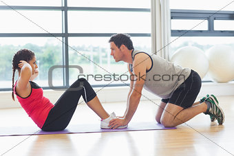 Trainer helping woman do abdominal crunches in gym