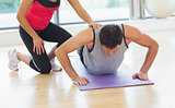 Female trainer assisting man with push ups in gym