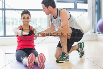 Male trainer assisting woman with pilate exercises in fitness studio