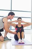 Trainer assisting woman with pilate exercises in fitness studio
