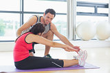 Trainer assisting woman with pilate exercises in fitness studio