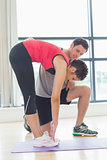 Male trainer assisting woman with stretching exercises in fitness studio