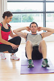 Female trainer watching man do abdominal crunches  on exercise mat