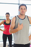 Fit man holding water bottle with friend in background in exercise room