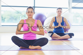 Two sporty women sitting with joined hands at fitness studio