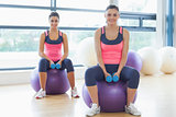 Two fit women with dumbbells on fitness balls in gym