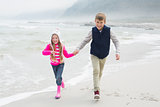 Happy brother and sister walking hand in hand at beach