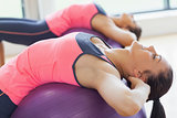 Two fit young women stretching on fitness balls in gym