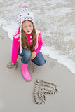 Little girl with drawn heart shape on sand at beach