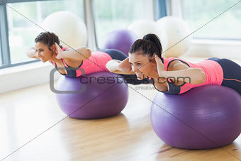 Two fit women exercising on fitness balls in gym