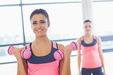 Fit woman lifting dumbbell weights with friend in background at gym