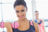 Woman lifting dumbbell weight with friend in background at gym