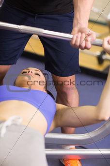 Trainer helping woman to lift the barbell bench press in gym