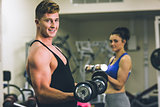 Young man and woman using dumbbells in gym