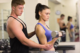Male trainer helping woman with the dumbbells in gym