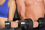 Mid section of a shirtless man and woman with dumbbells