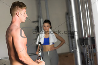 Woman looking at determined man use the lat machine in gym