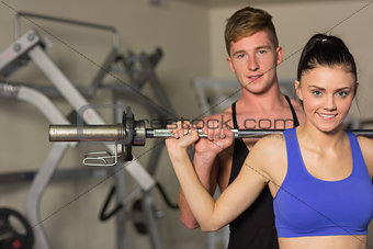 Male trainer helping fit woman to lift the barbell in gym