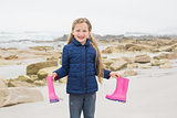 Cute smiling girl holding her wellington boots at beach