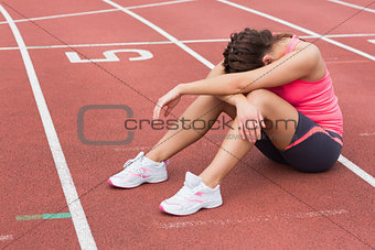 Tensed sporty woman sitting on the running track