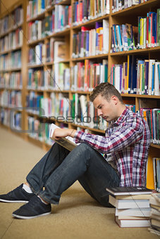 Serious student sitting on library floor reading