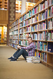 Cheerful student sitting on library floor reading