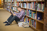 Focused young student sitting on library floor using tablet