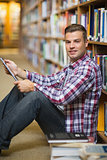 Smiling young student sitting on library floor using tablet