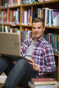 Happy young student sitting on library floor using laptop