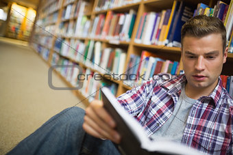 Serious young student sitting on library floor reading book