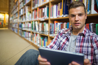 Young student sitting on library floor using tablet