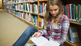 Young pretty student sitting on library floor reading book