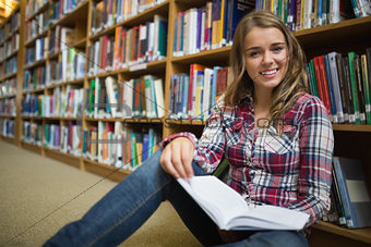 Happy pretty student sitting on library floor reading book