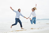 Cheerful couple holding hands and jumping at beach