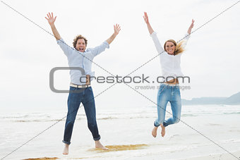 Cheerful young couple jumping at beach