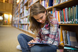 Pretty student sitting on library floor using tablet